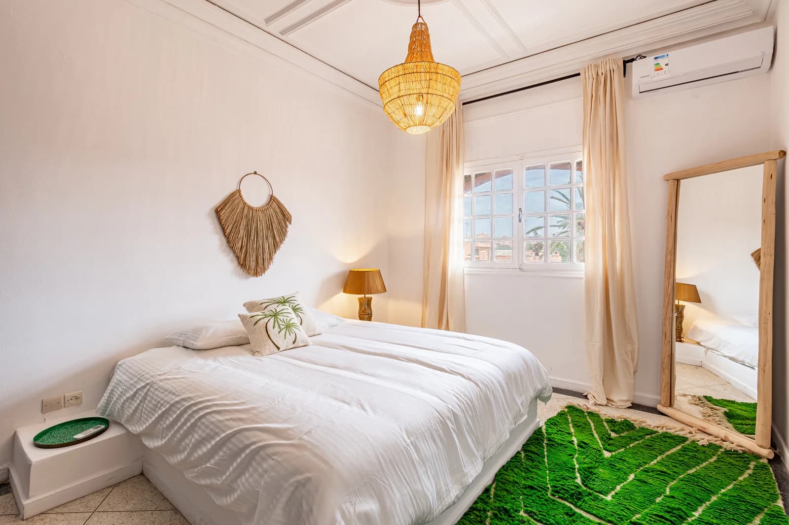 Bedroom with green Beni Ourain rug, wicker chandelier and arched window