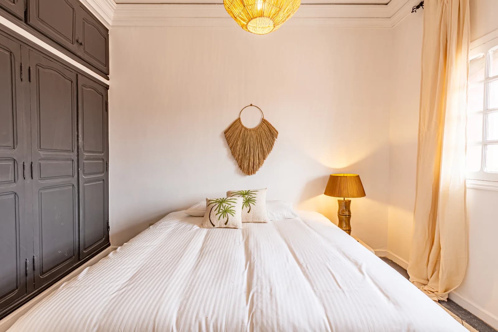 Second bedroom with golden lamp, jute fan art and dark armoire