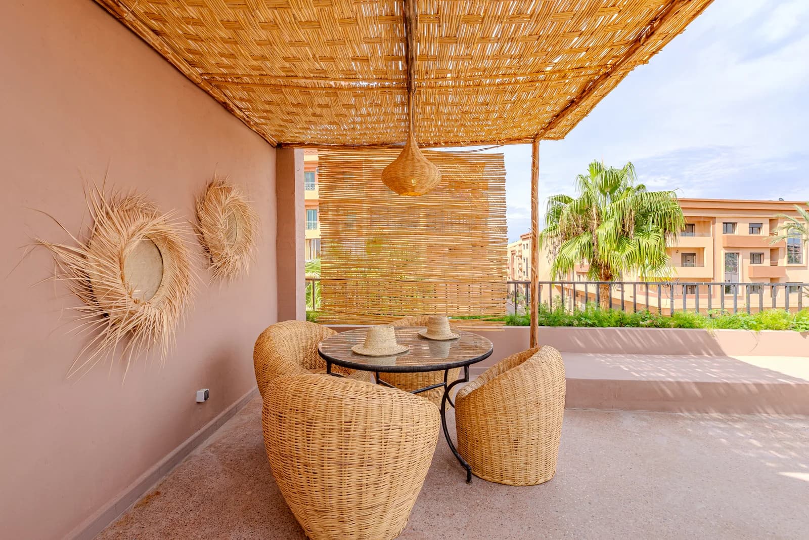 Pink-walled corner with wicker chairs, palm-frond mirrors and reed canopy
