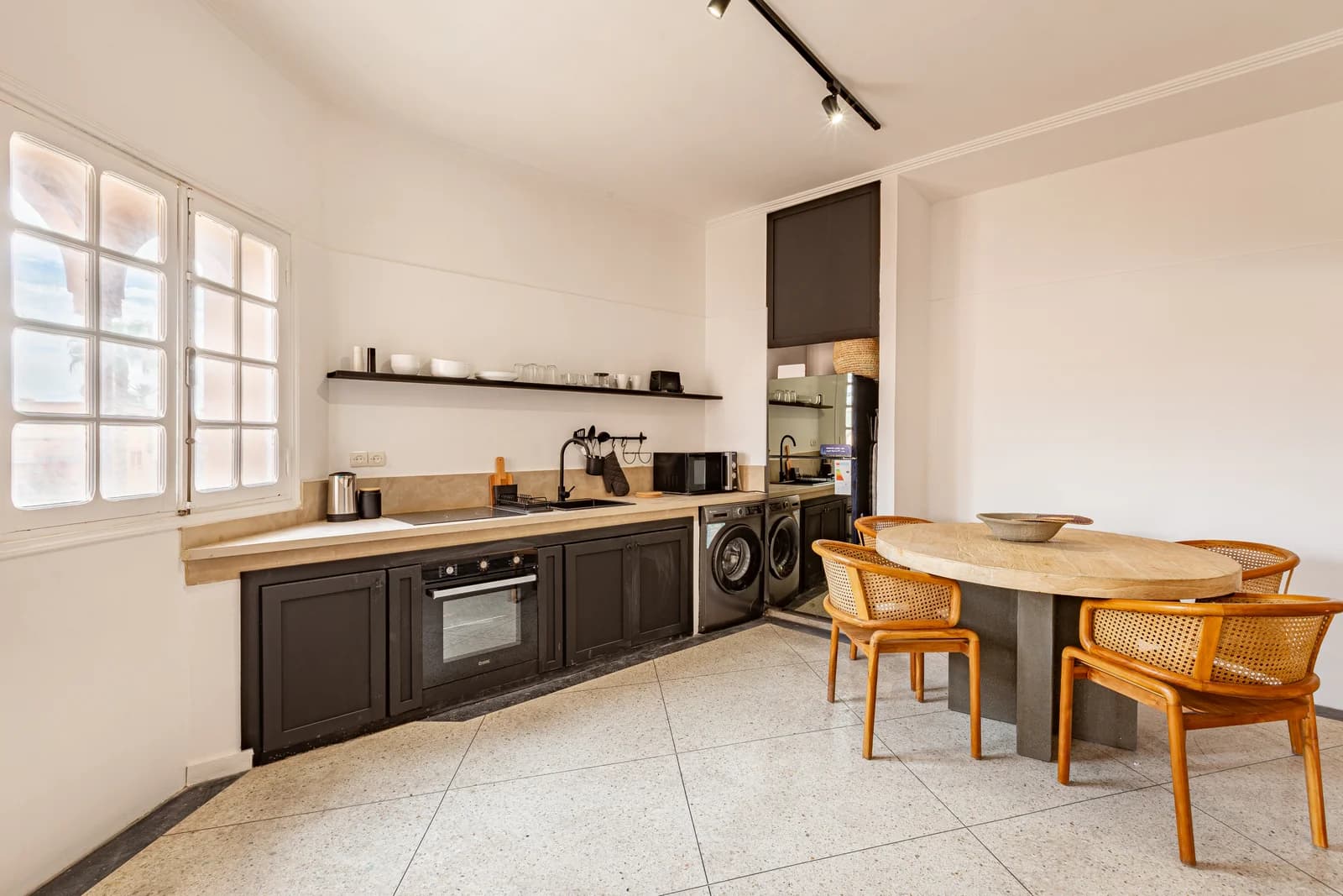Black-and-wood kitchen with cane-back chairs and bright shuttered window