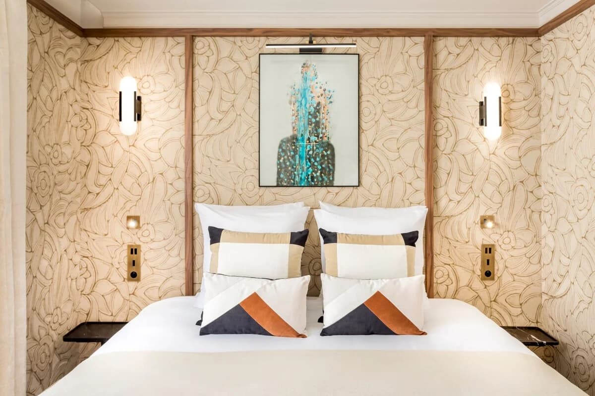Bed framed by carved walnut headboard, embossed wallpaper and twin sconces