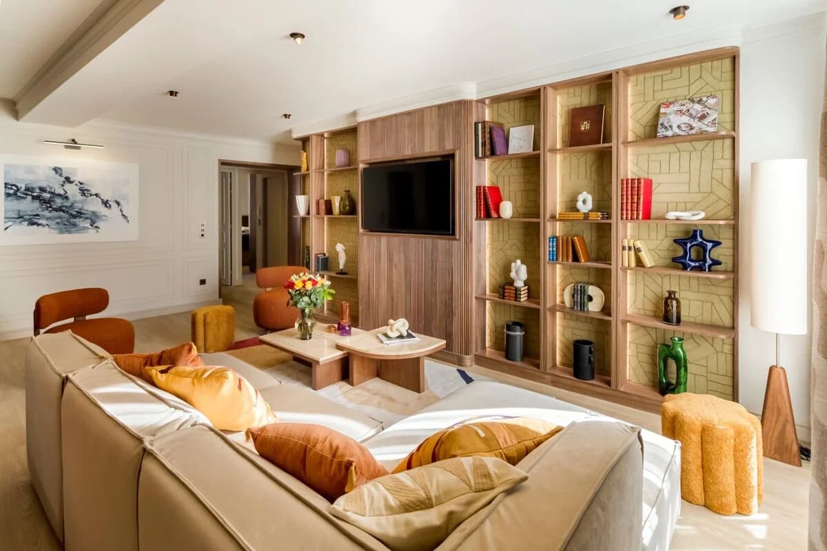 Wide lounge view across pillowed sectional toward sculpted bookshelves