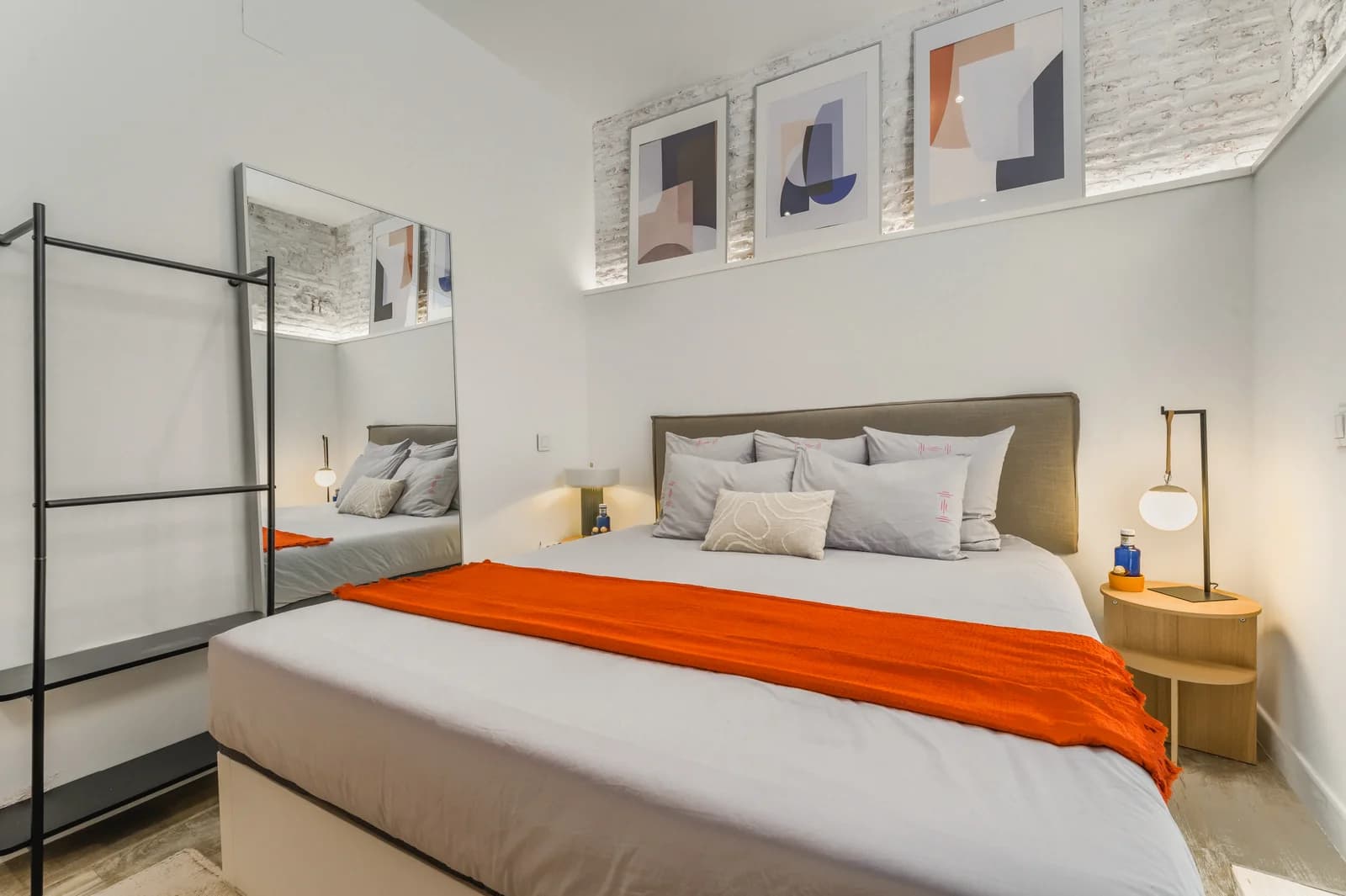 Bedroom with abstract triptych prints, brass lamps and orange throw