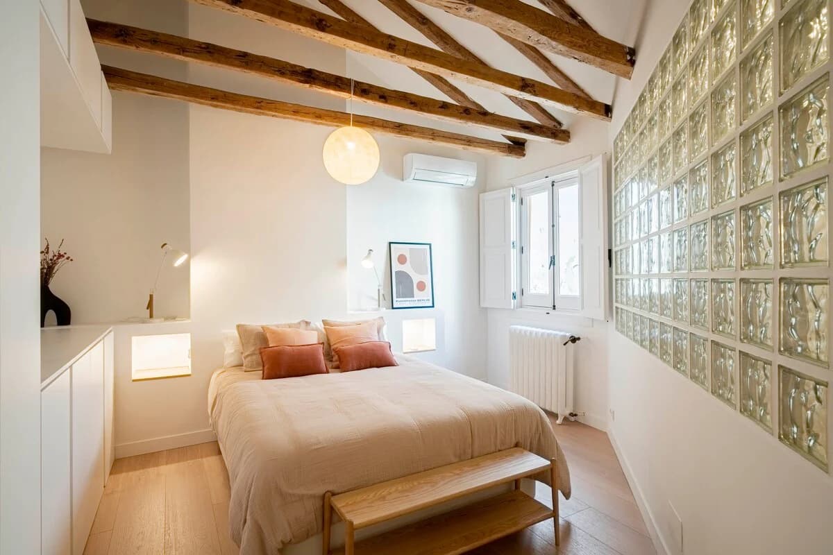 Beamed bedroom with glass-block wall, terracotta cushions and globe pendant