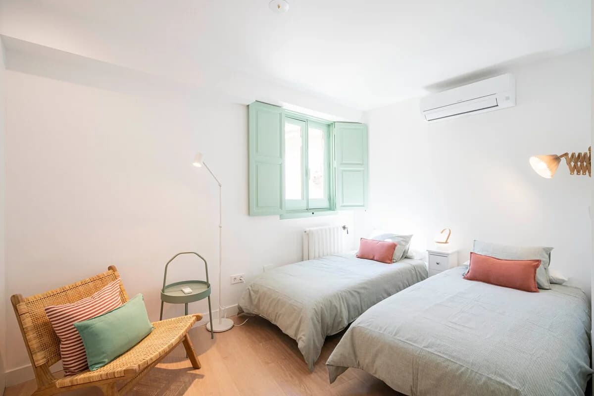 Twin bedroom with mint shutters, rattan chair and soft striped linens