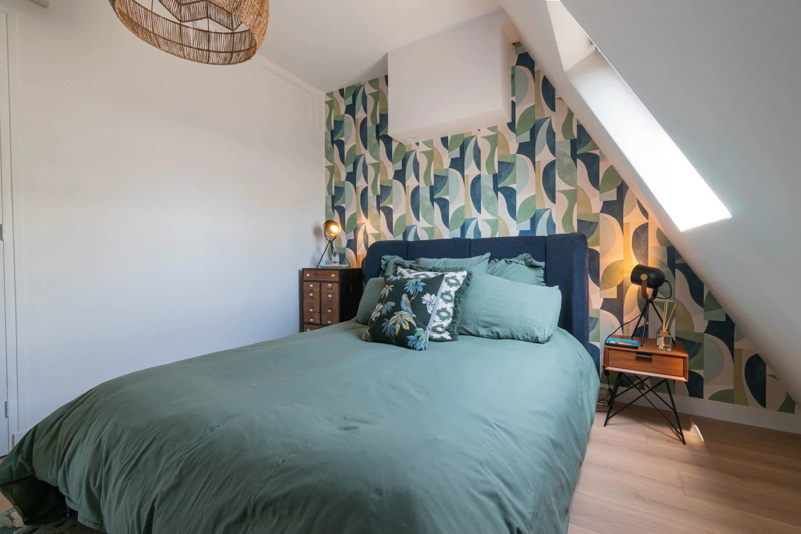 Eaved bedroom with bold leaf wallpaper and emerald linen bedding