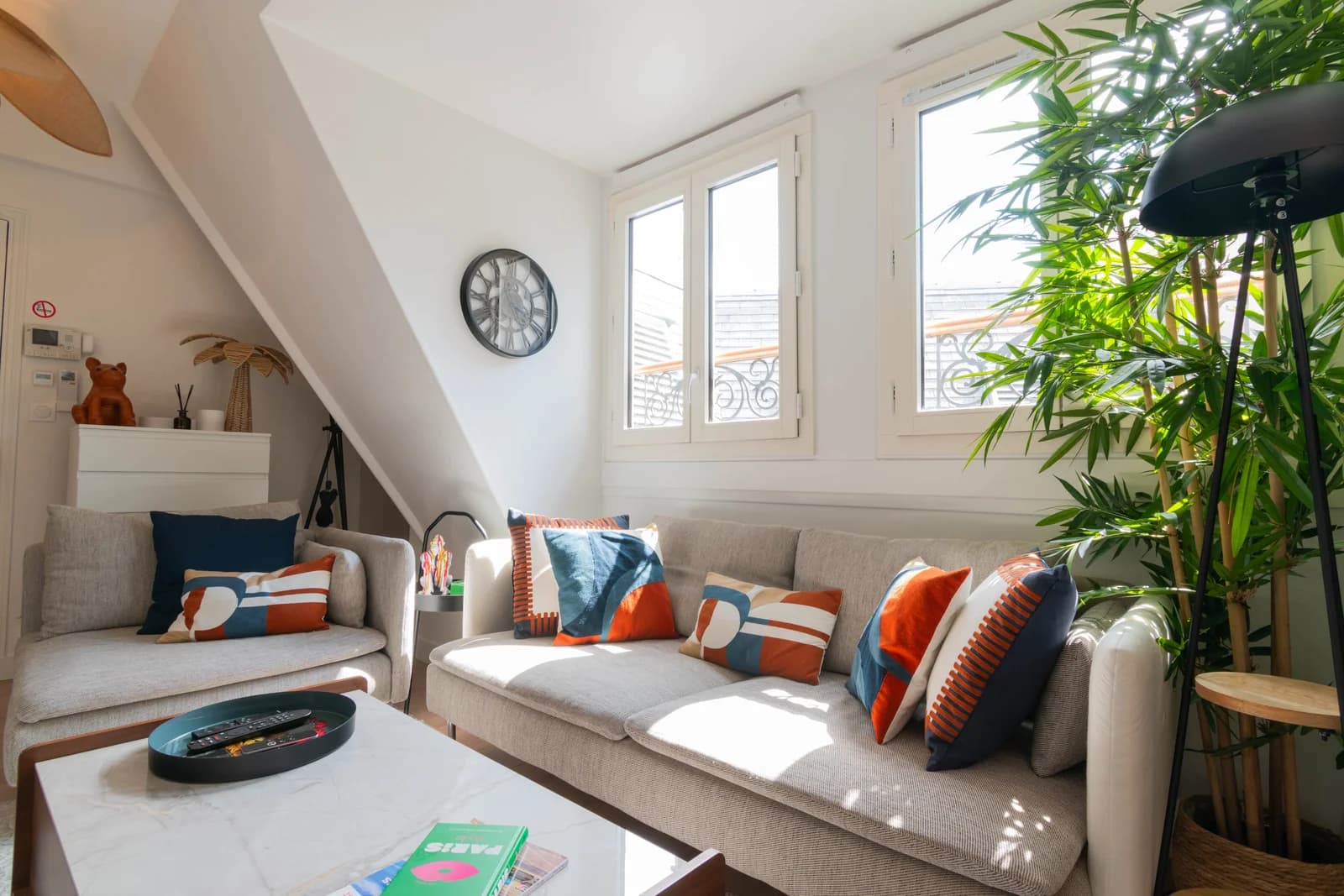 Cushion-lined sofa under triple windows with bamboo plant and clock