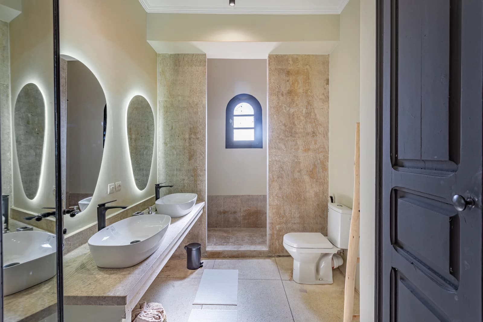 Tadelakt bathroom with twin oval mirrors and arched moroccan window