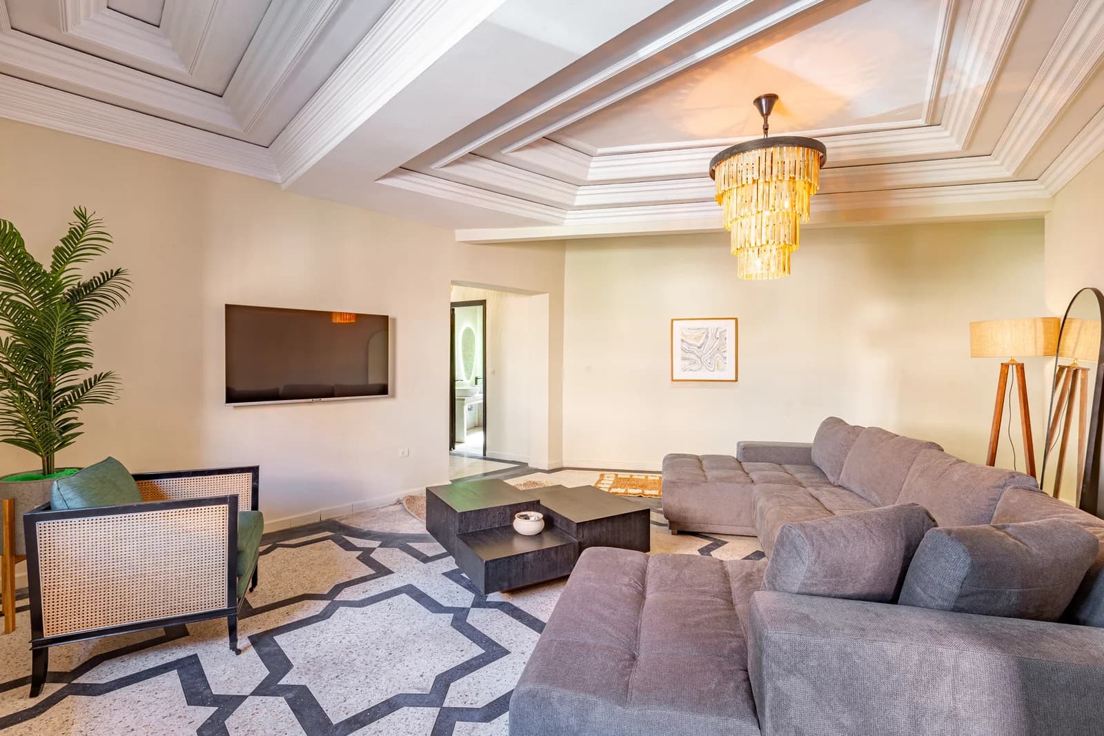 Grand living room under coffered ceiling with crystal chandelier and patterned floor