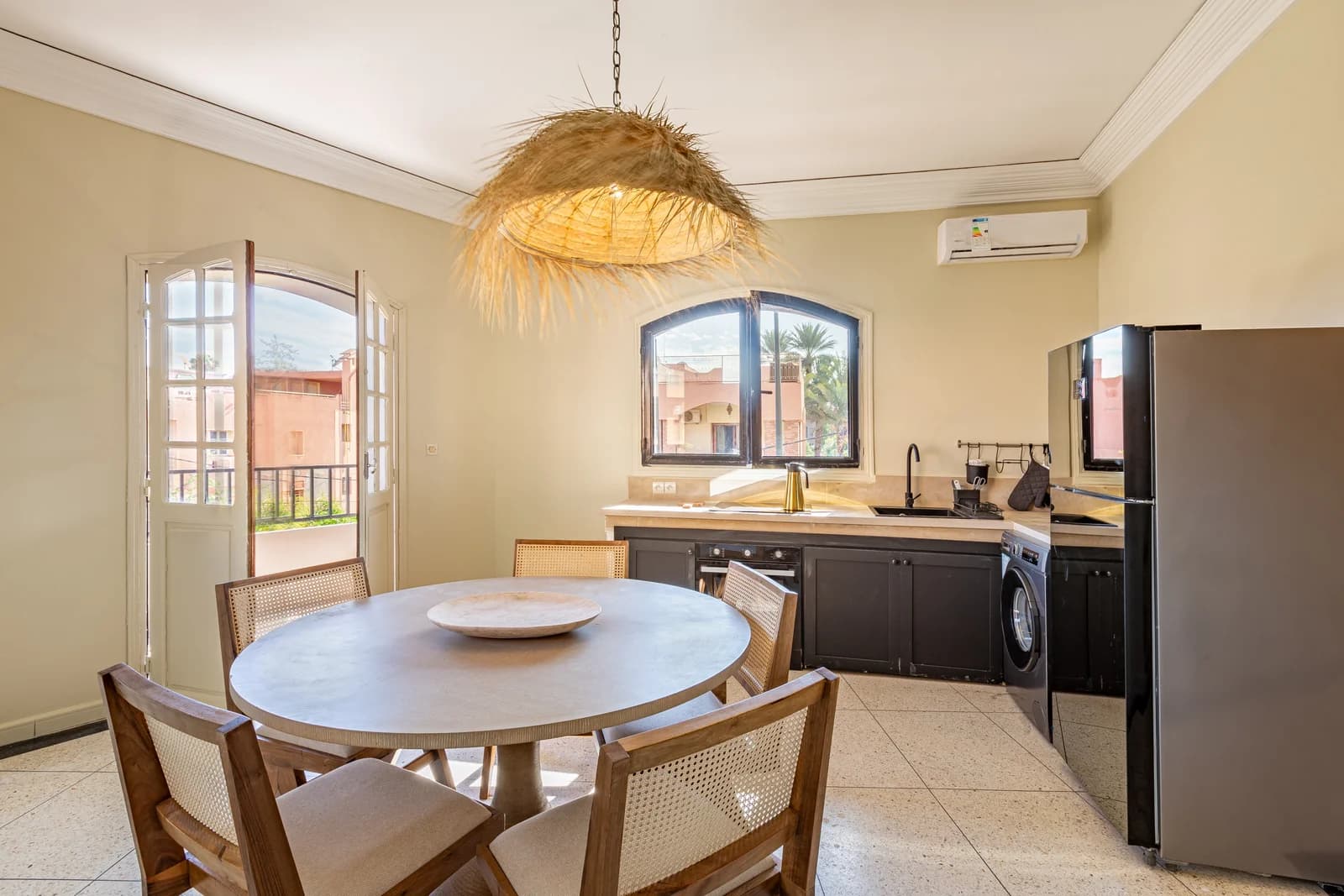Open kitchen with cane chairs, palm view and oversized straw pendant