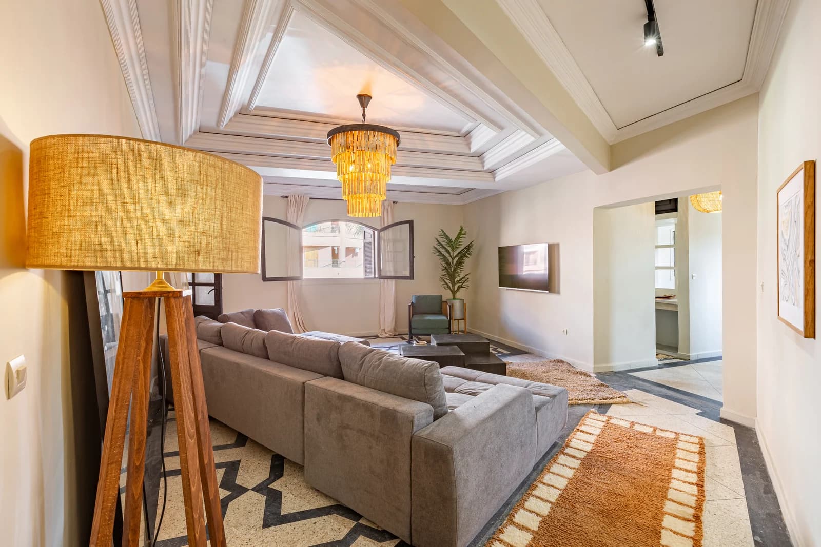 Coffered-ceiling lounge with golden chandelier and grey velvet sectional