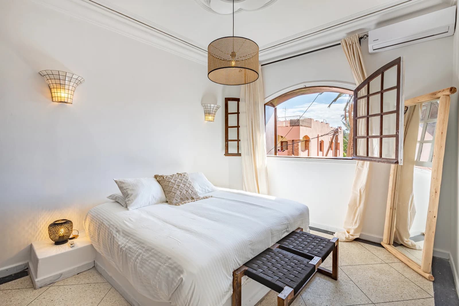 Bedroom with arched window framing palm trees and Marrakech rooftops