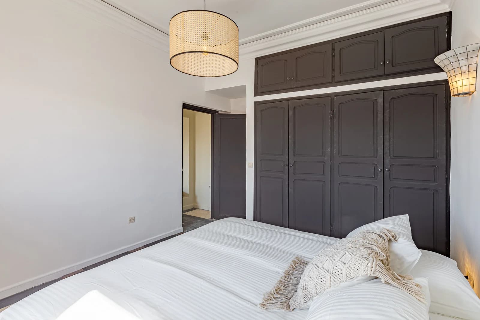 Carved black-painted wardrobe doors framing serene white bedroom
