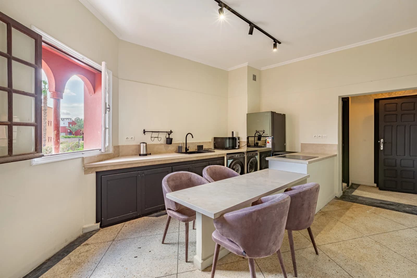 Eat-in kitchen with mauve velvet chairs and arched window onto courtyard