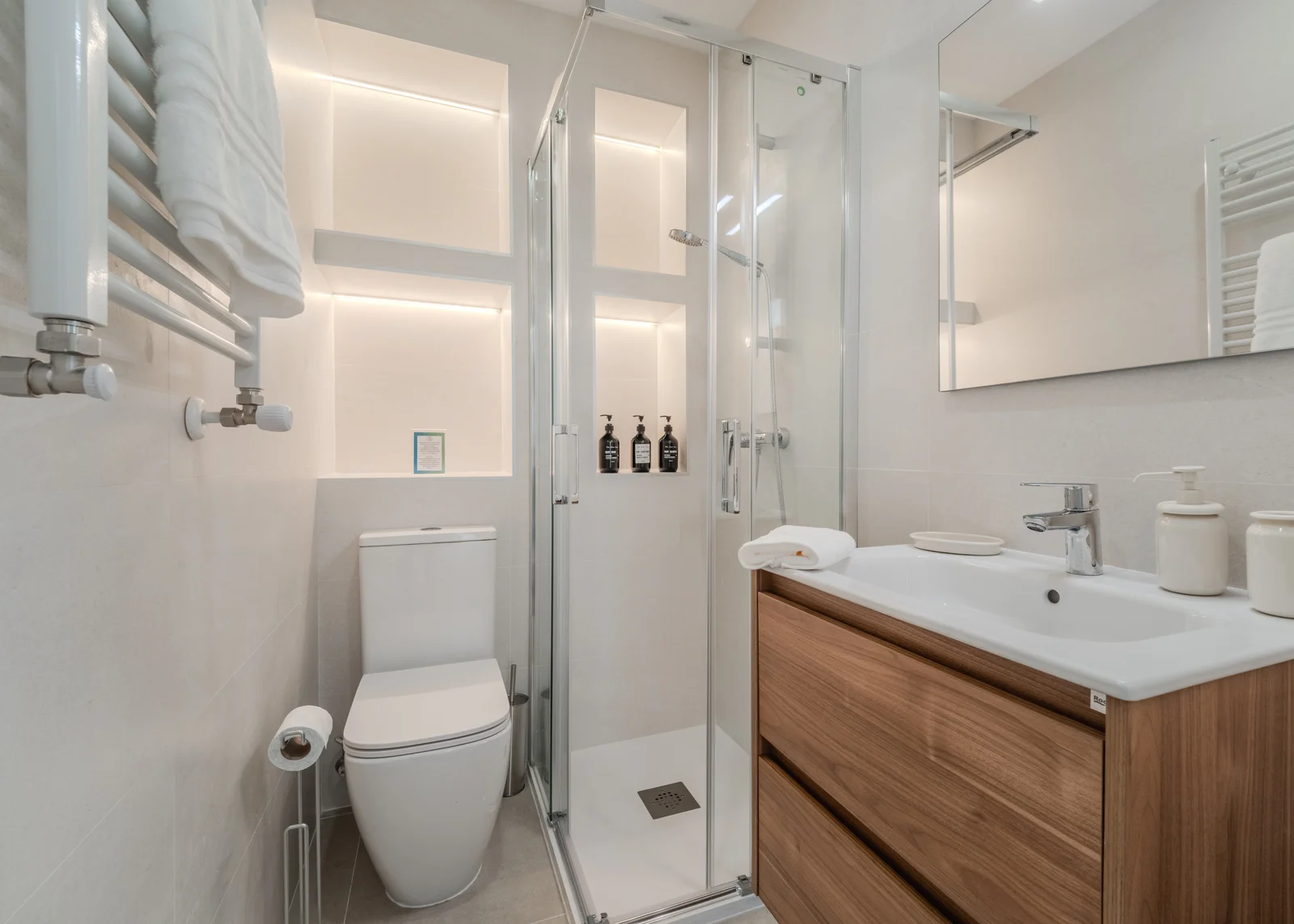 Compact bathroom with walnut vanity, glass shower and recessed shelf