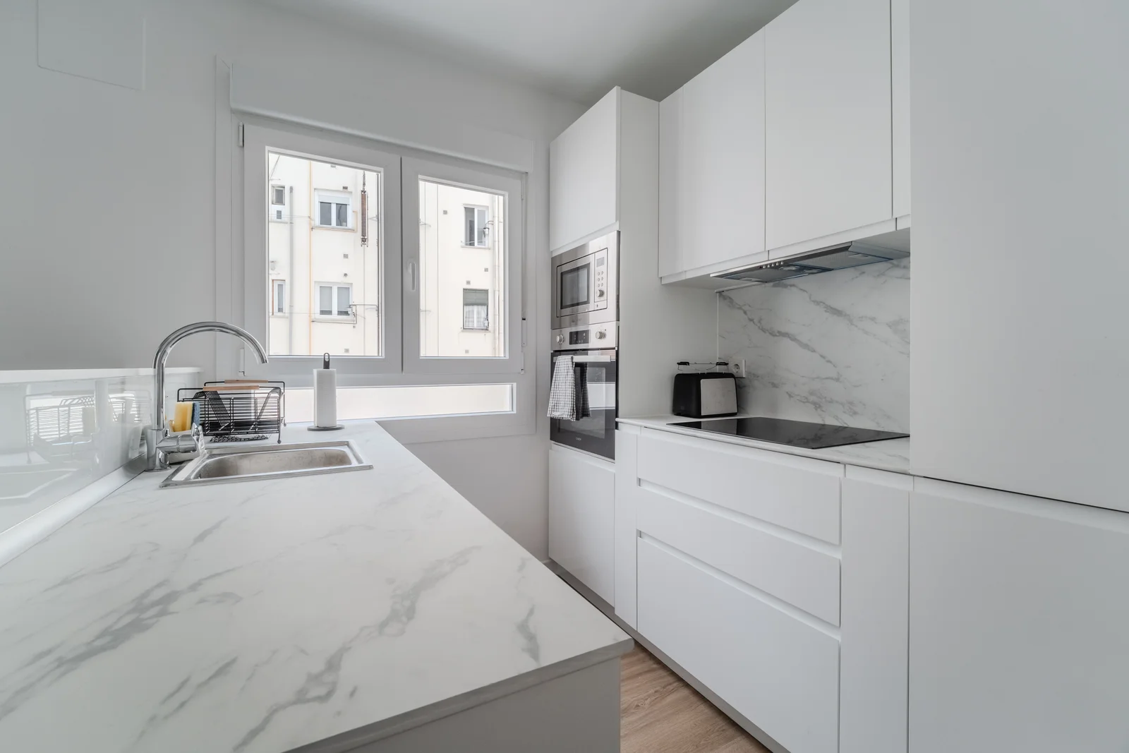 Crisp white kitchen with marble counters, induction hob and oven tower