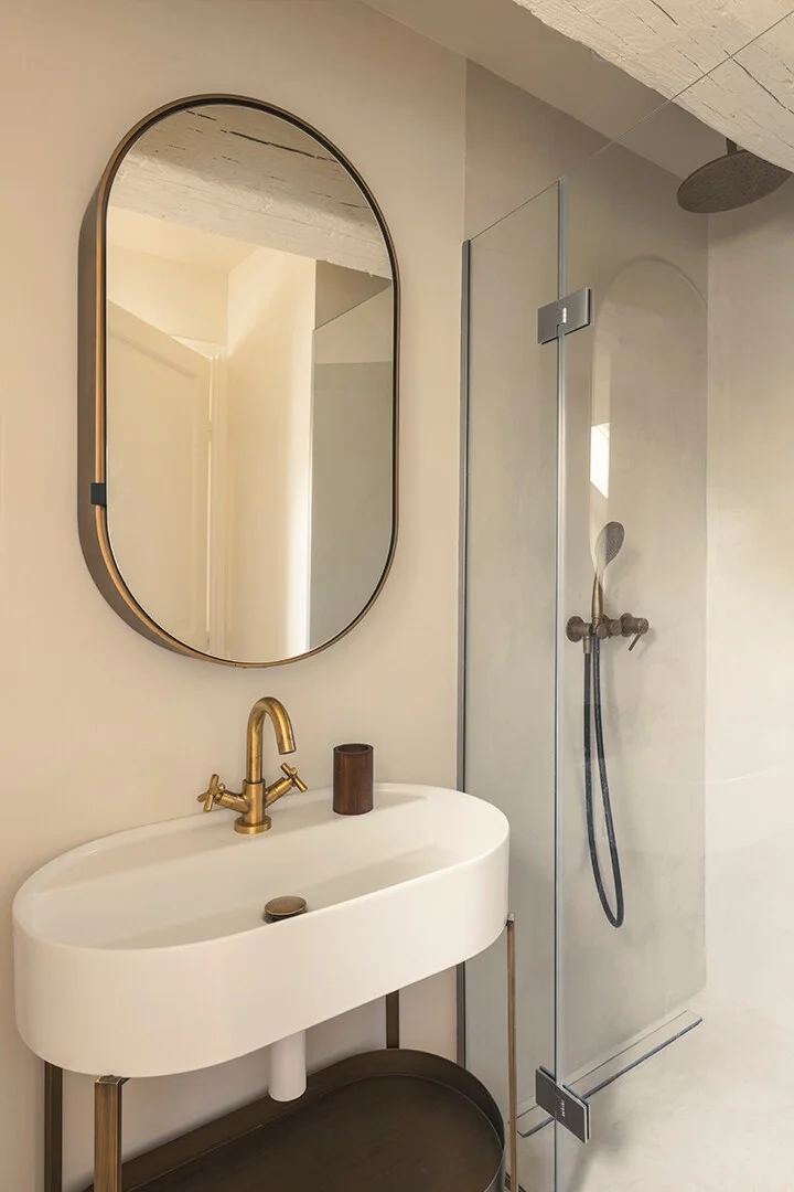 Plaster-walled bathroom with brass tap and oval pill mirror