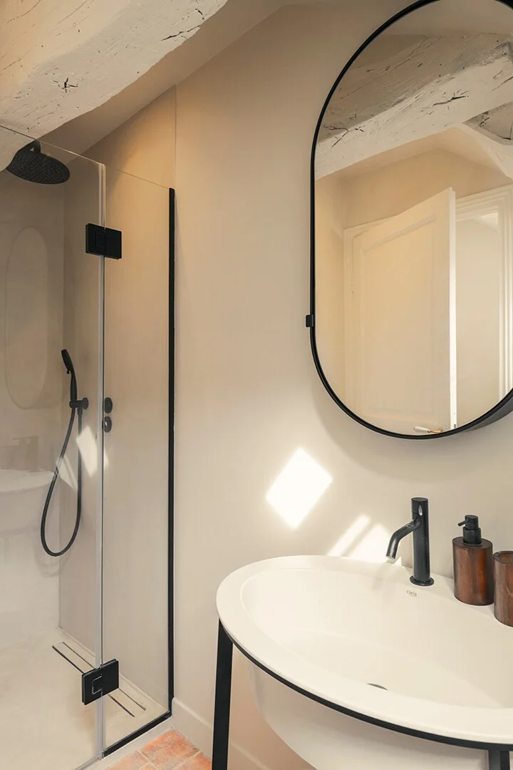 Limewashed bathroom with rain shower and oval black-framed mirror