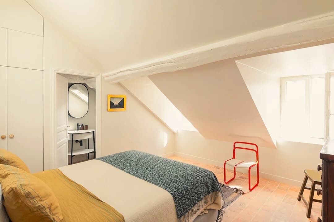 Loft bedroom with mustard linens, beam ceiling and ensuite peek