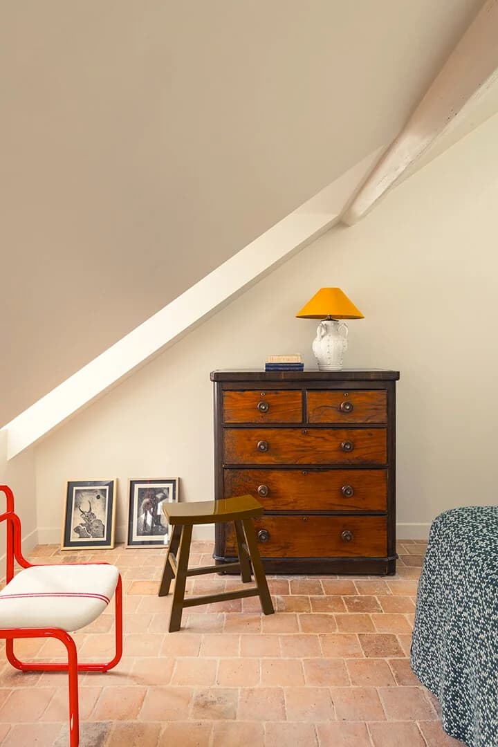 Antique dresser with yellow lamp and framed prints on terracotta floor