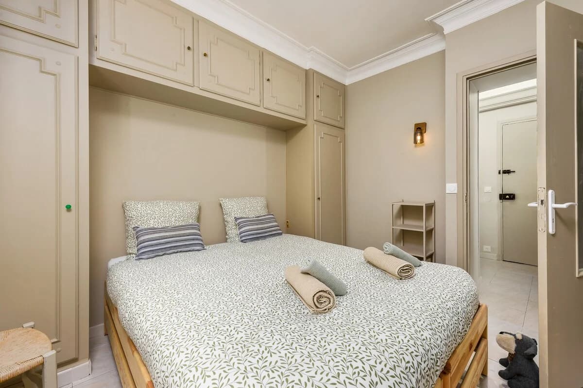 Built-in cabinetry above bed with botanical linens and brass sconce