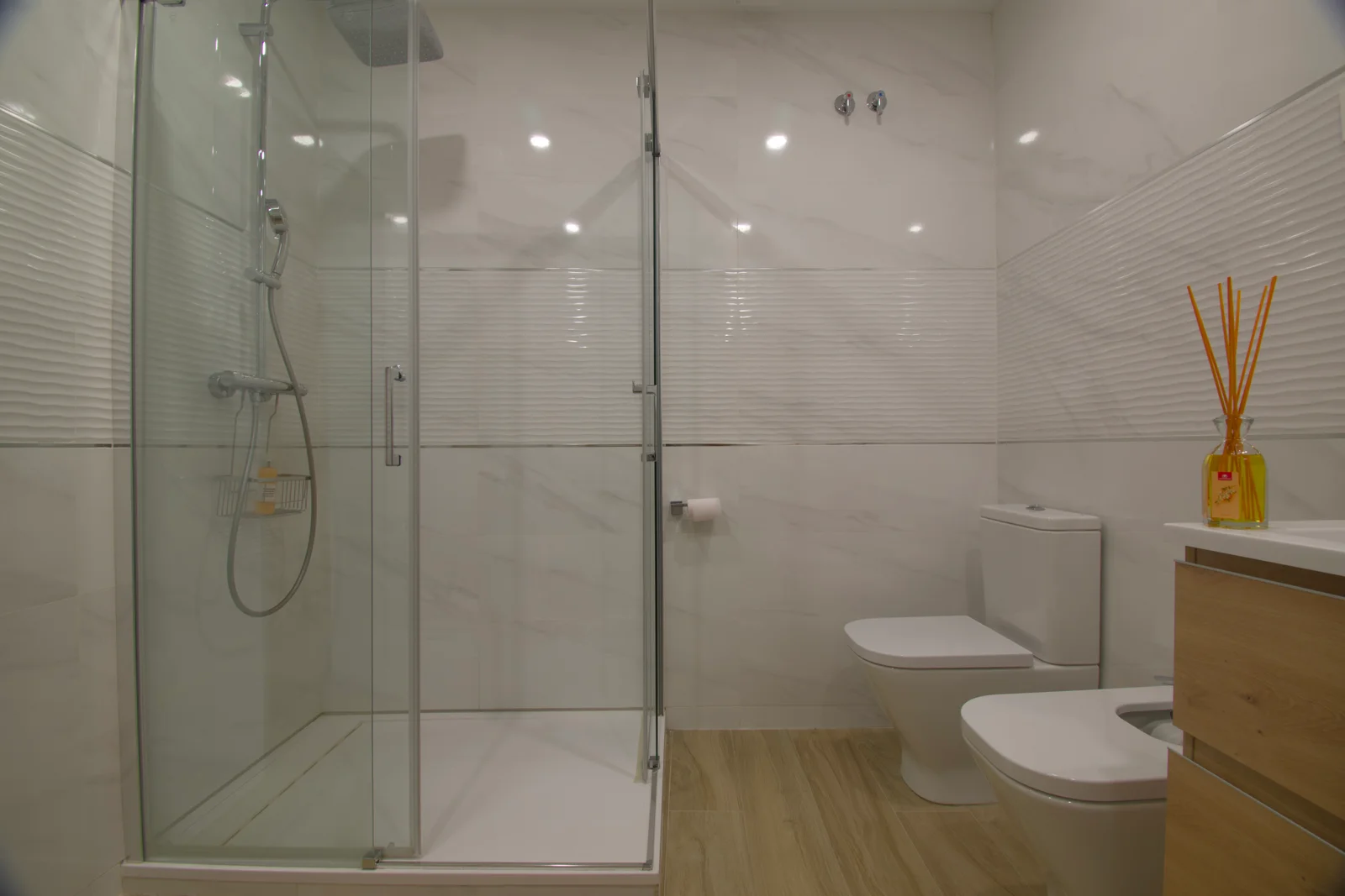 Glass-enclosed shower paired with marble toilet alcove