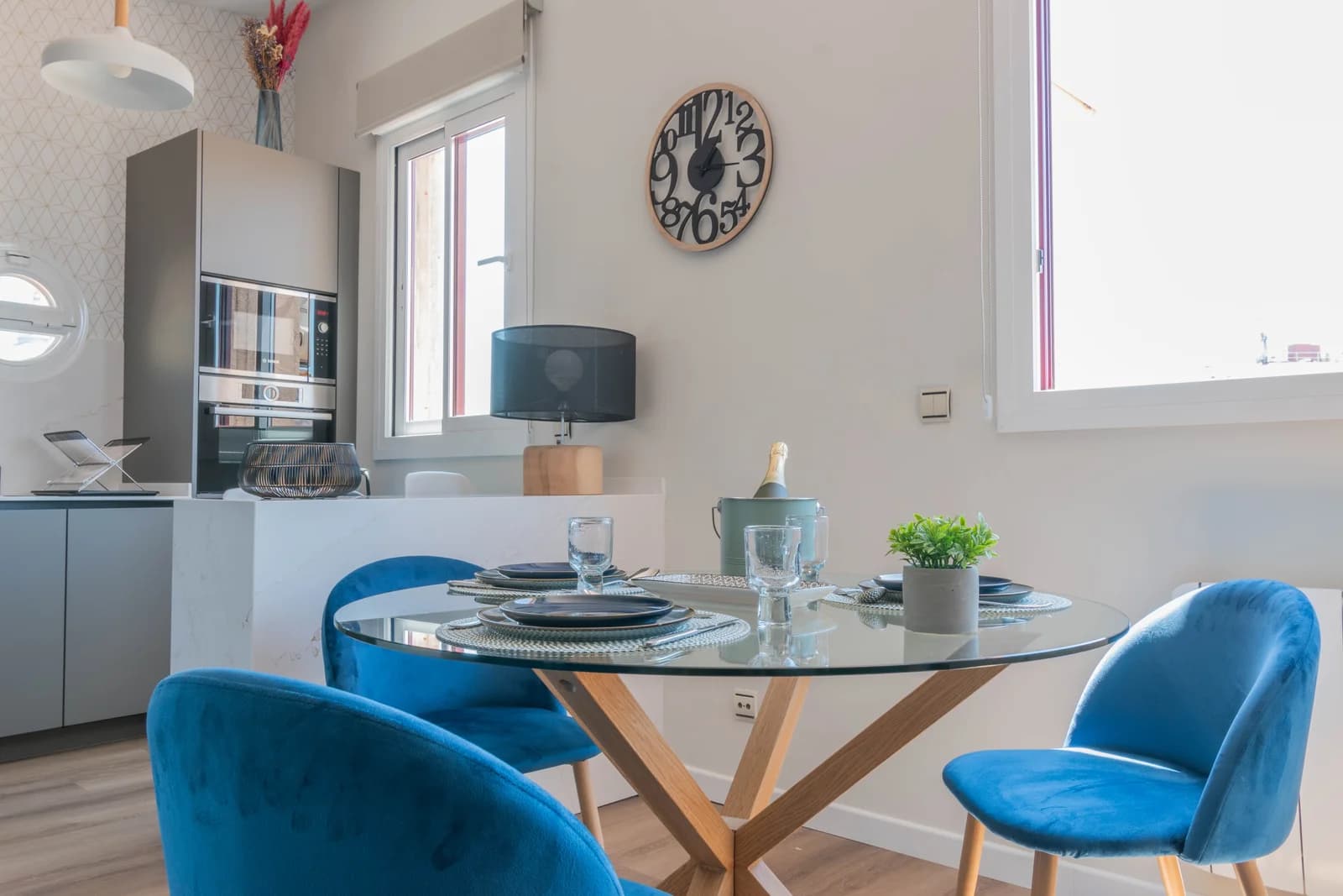 Glass dining table with velvet blue chairs beneath statement clock