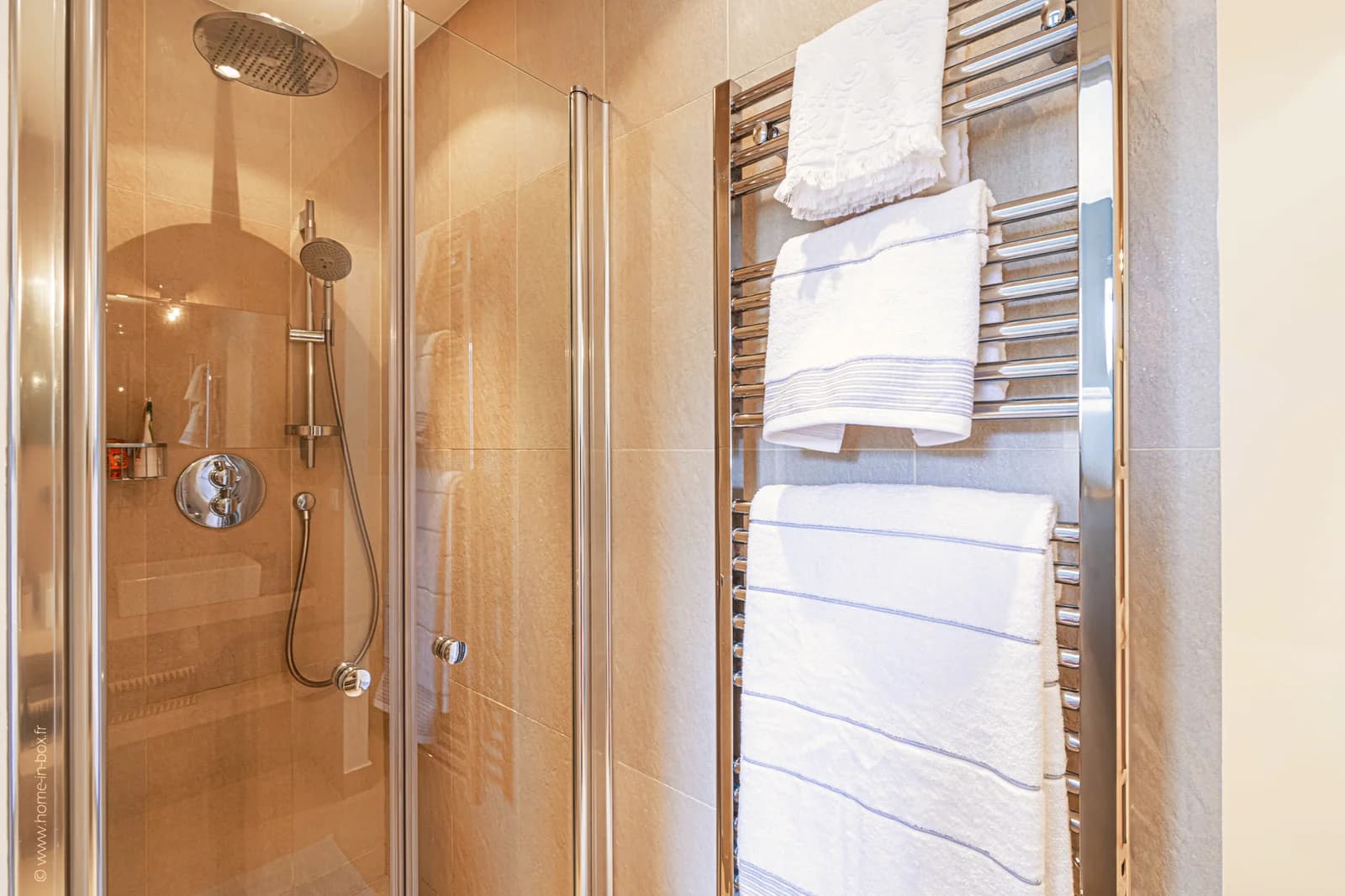 Glass shower stall with chrome heated towel rack and folded linens