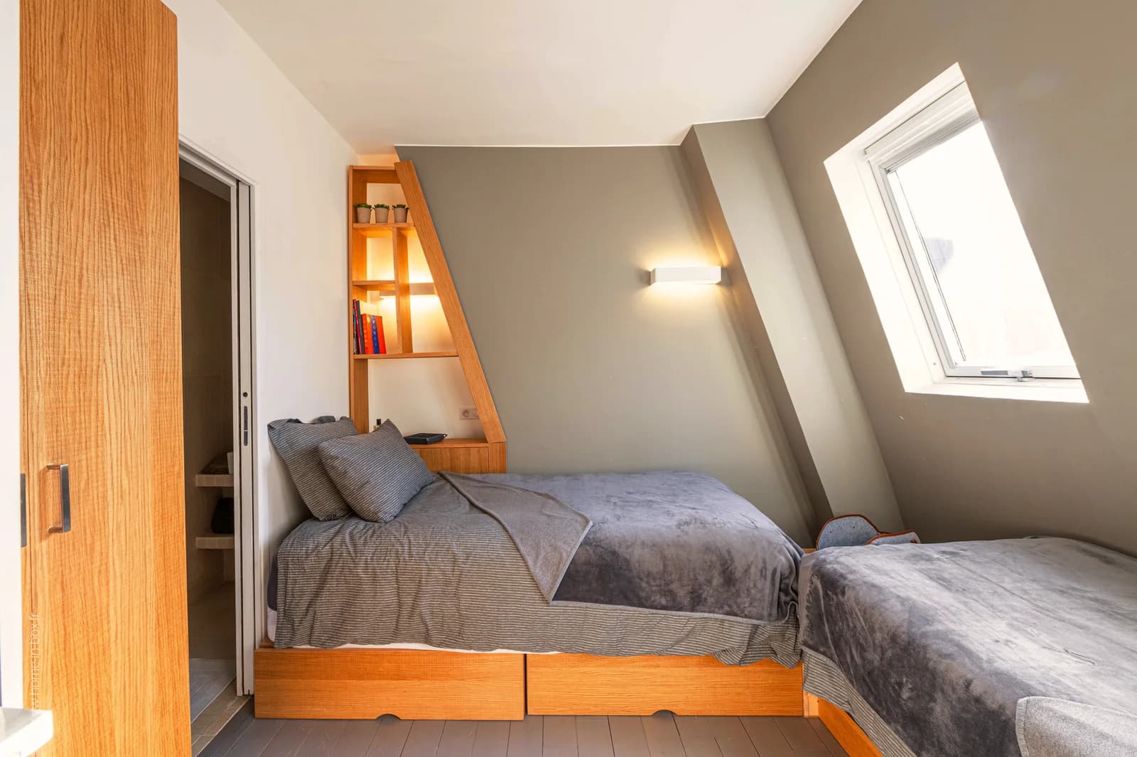 Twin beds tucked under angled ceiling with built-in bookshelf