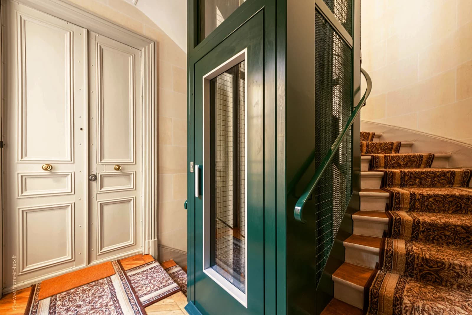 Emerald lift cage beside carpeted spiral staircase in classic stairwell