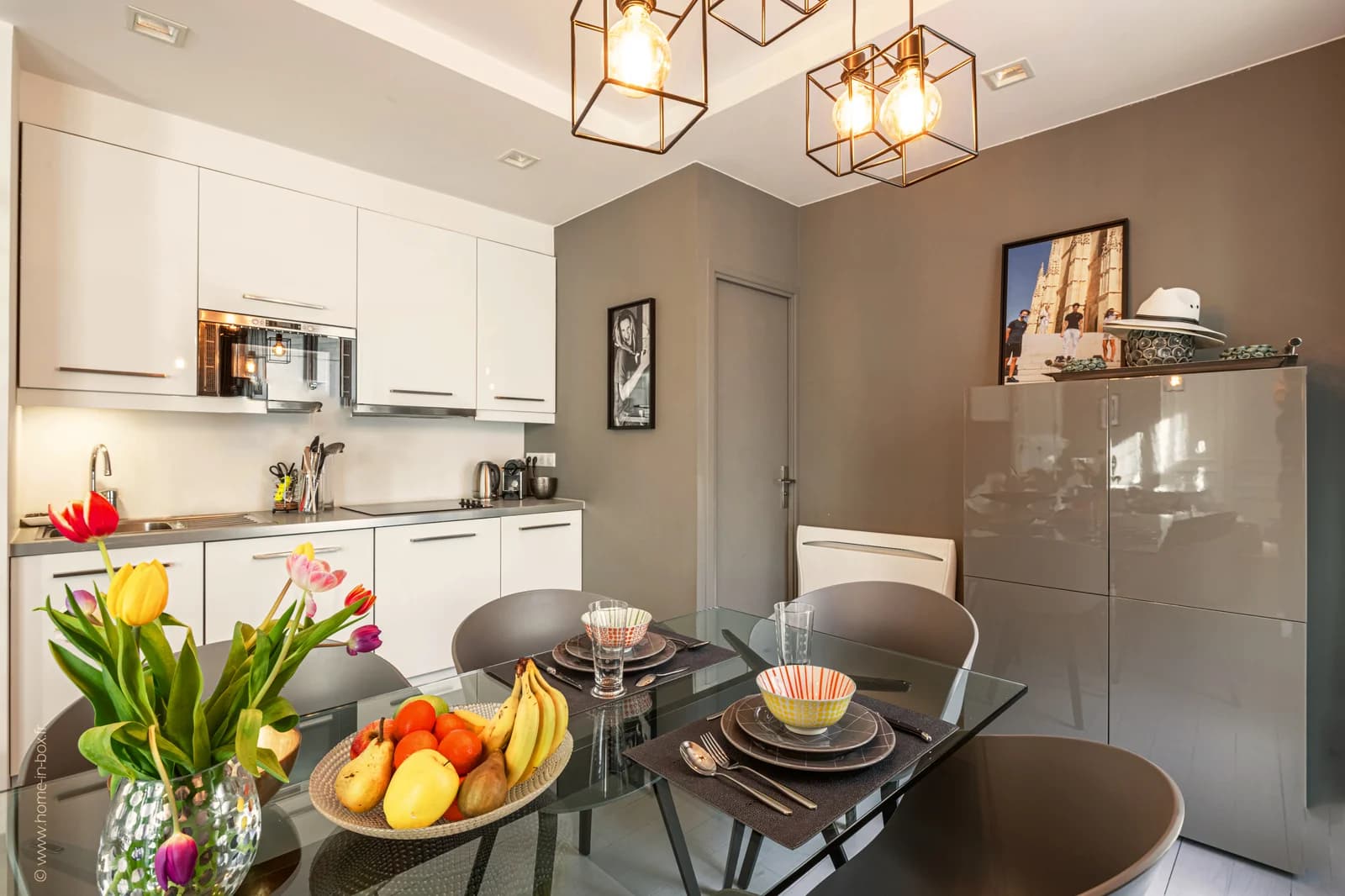 White kitchen meeting glass dining table beneath geometric pendants