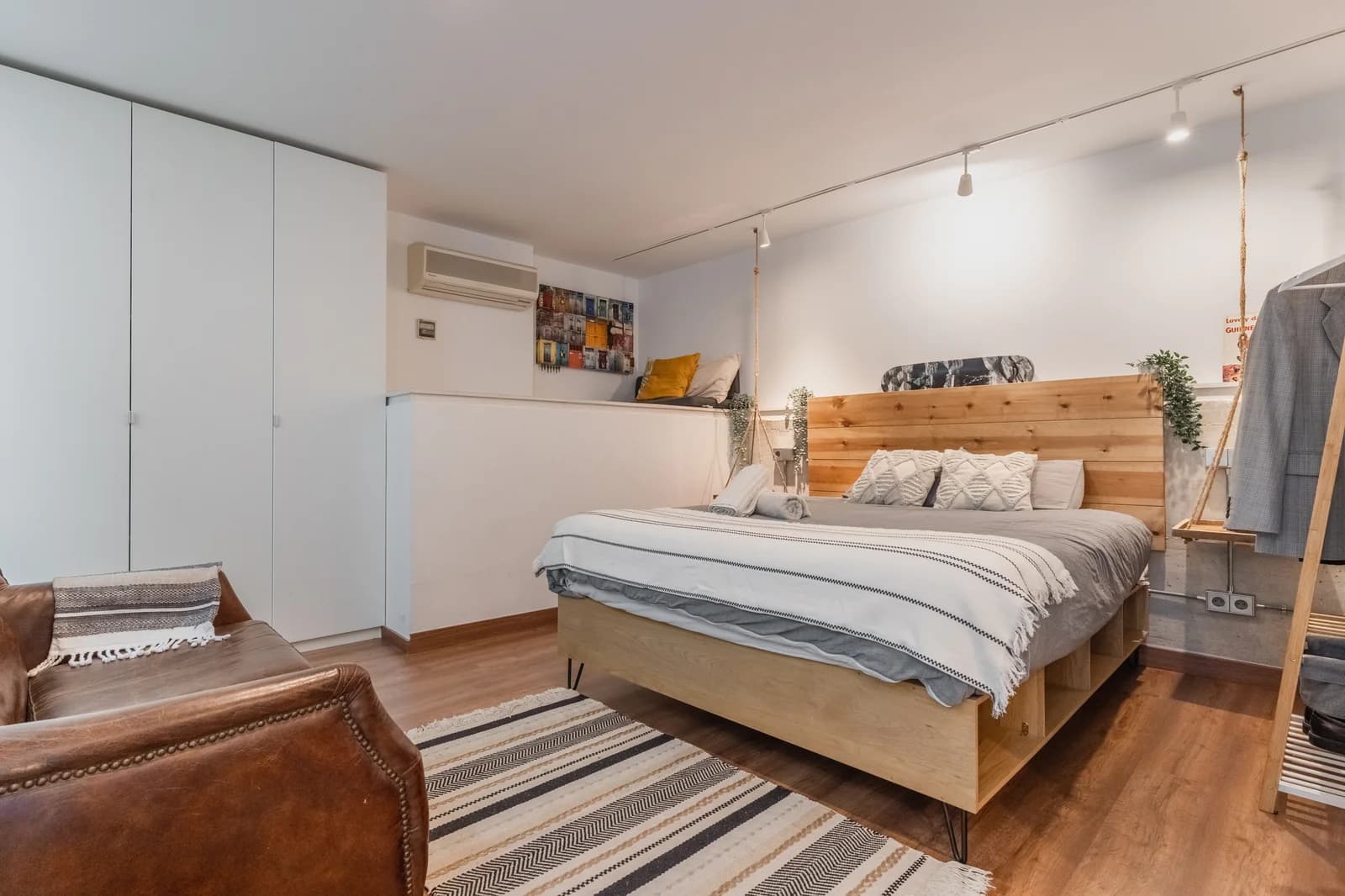 Loft bedroom with timber headboard, leather sofa, and striped rug
