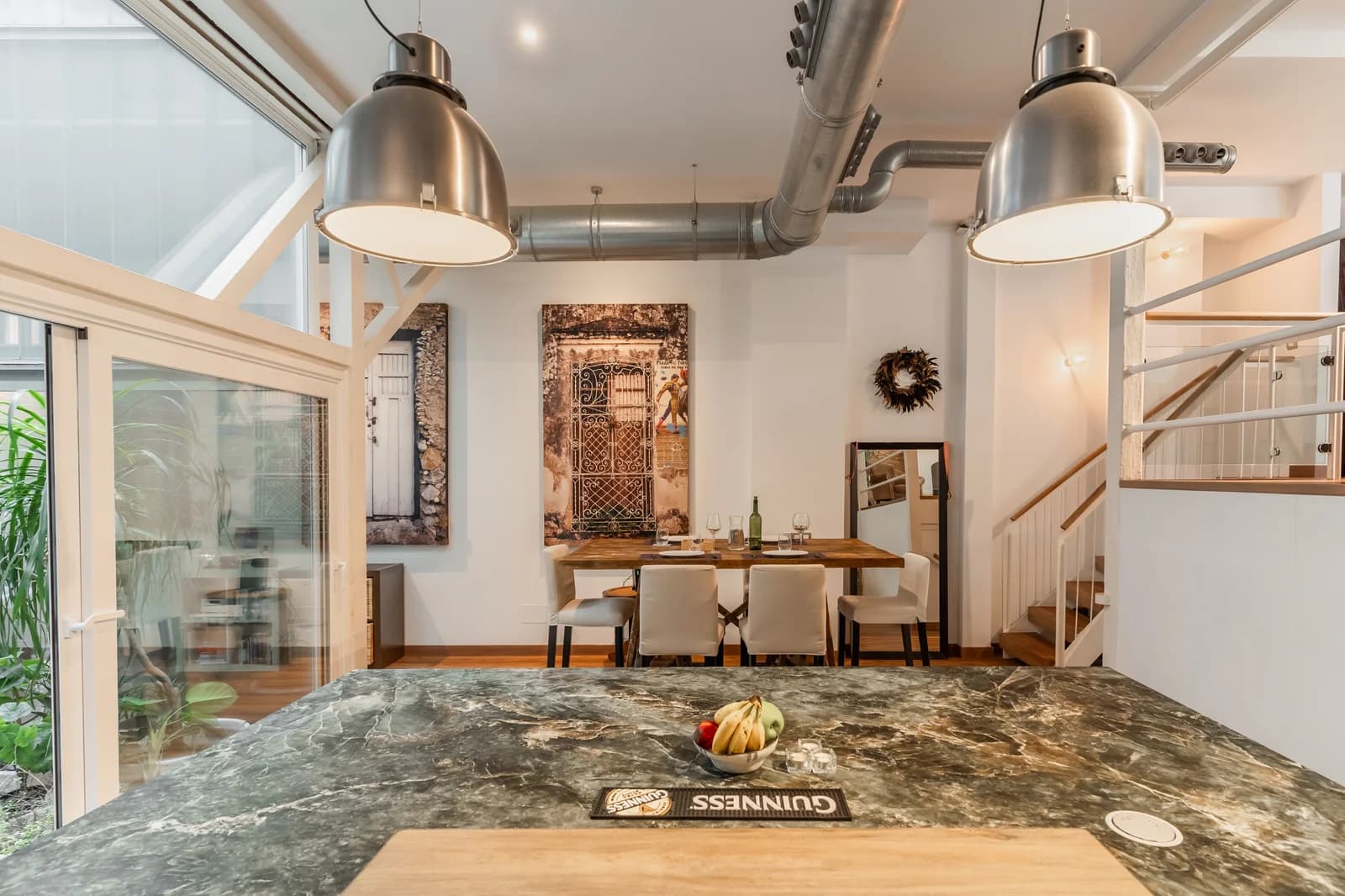 Industrial pendants over rustic dining table beside open stairs