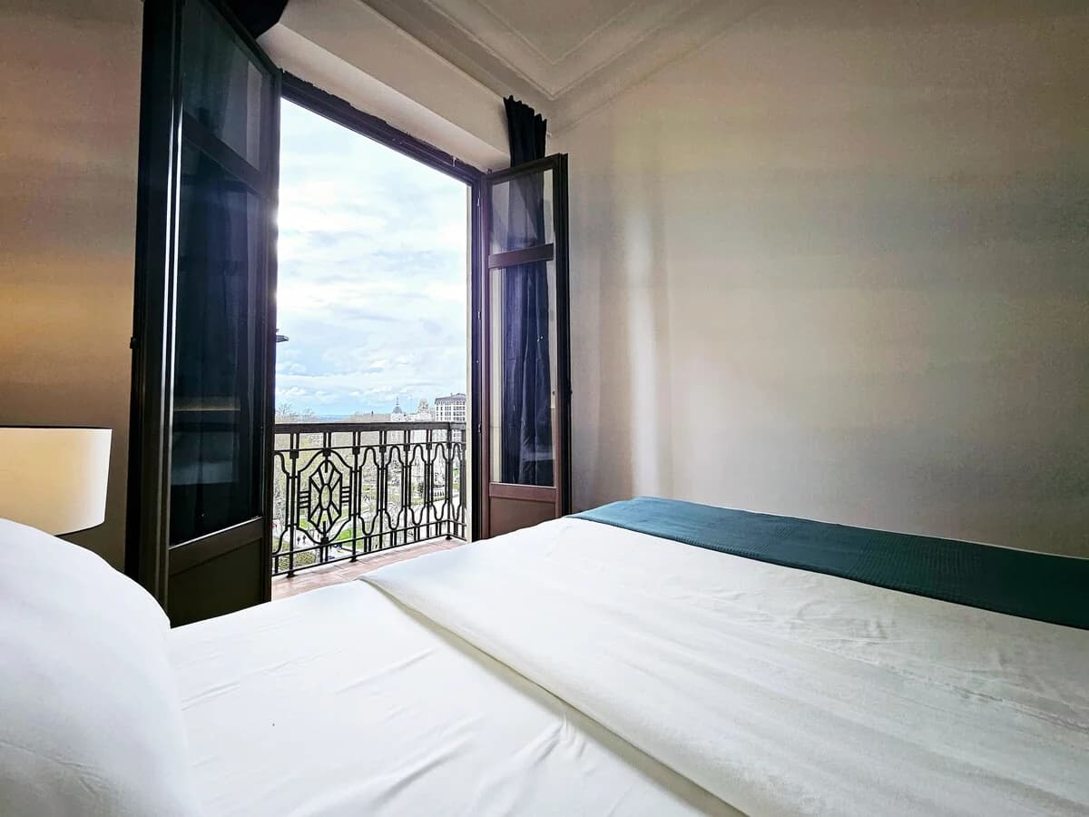 Bed framed by open balcony doors with city view beyond