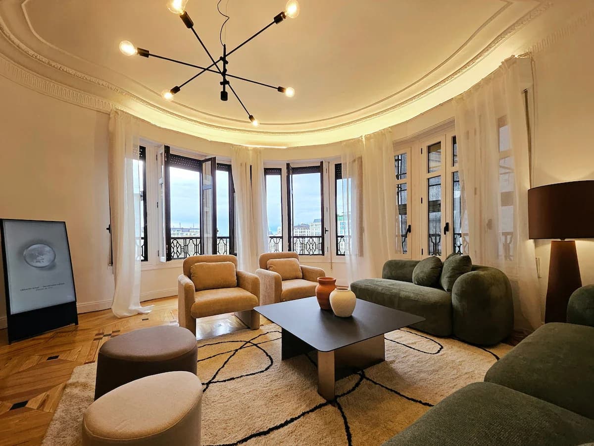 Curved-bay living room with green sofas under sputnik chandelier