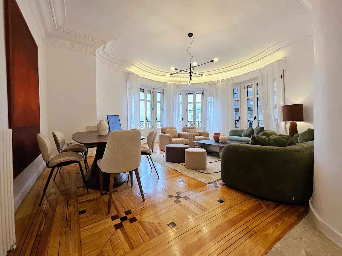 Living and dining together, sun pouring through tall bay windows
