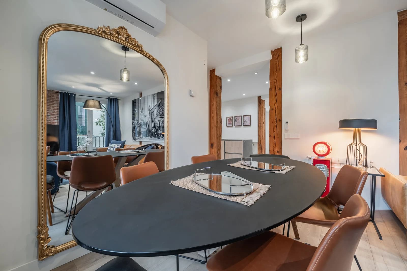 Dining oval table reflected in tall gilt mirror against brick column