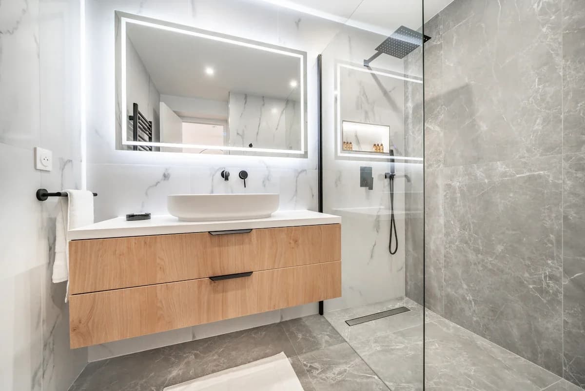 Marble bathroom with backlit mirror and walk-in stone shower