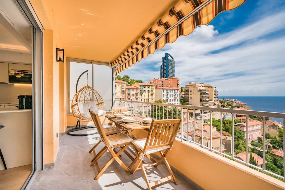 Striped-awning balcony with hanging rattan chair and sea-view dining