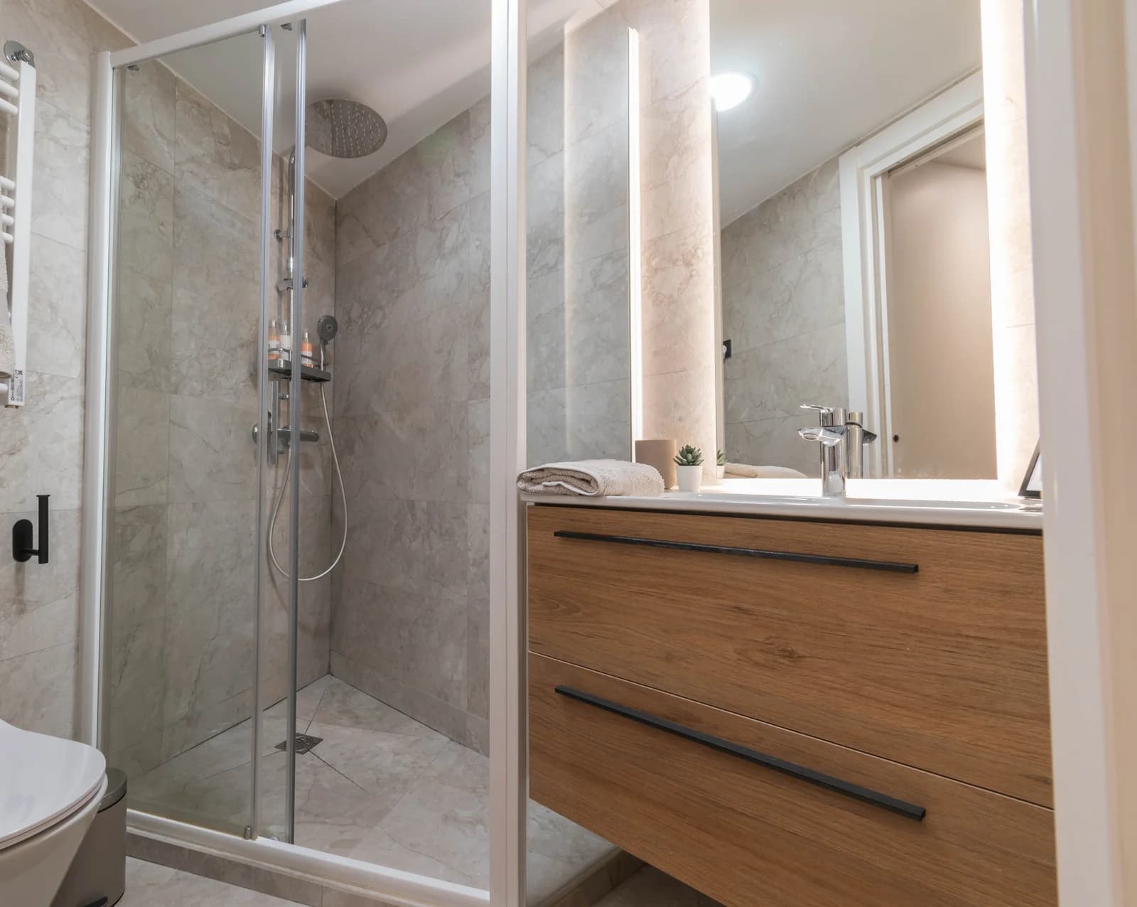 Bathroom looking from shower toward backlit mirror and wood vanity