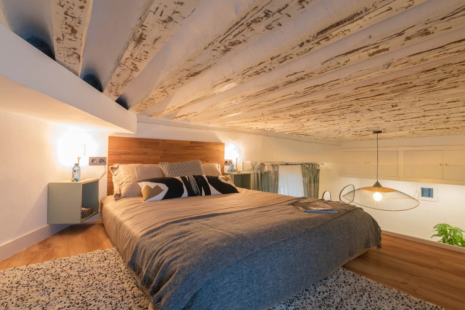 Loft bedroom under whitewashed wood-beam ceiling with pendant lamp