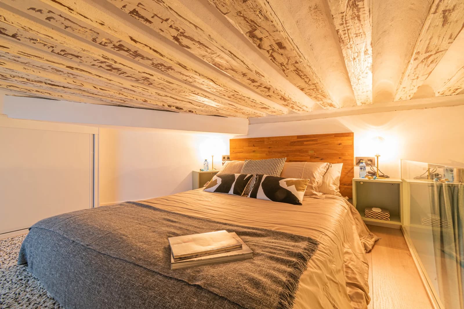 Cozy mezzanine bed nook with timber-beam ceiling and warm lighting