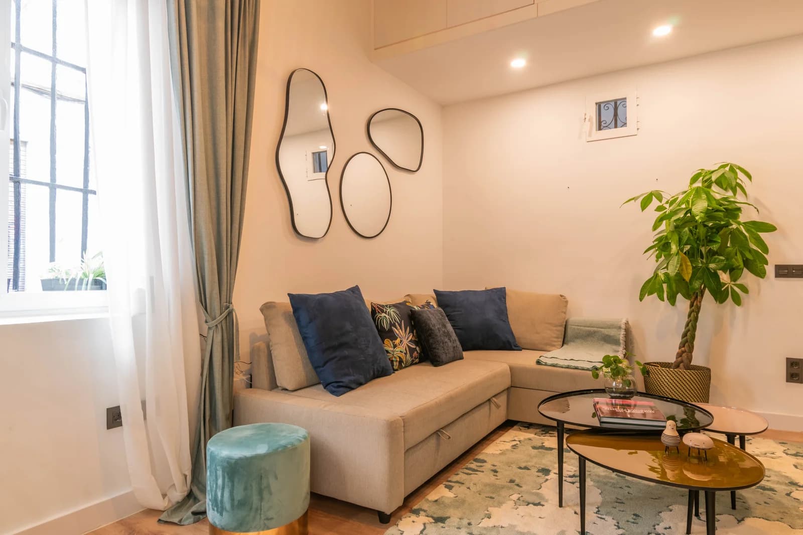 Sofa nook beneath shapely mirror trio with daylight from arched window