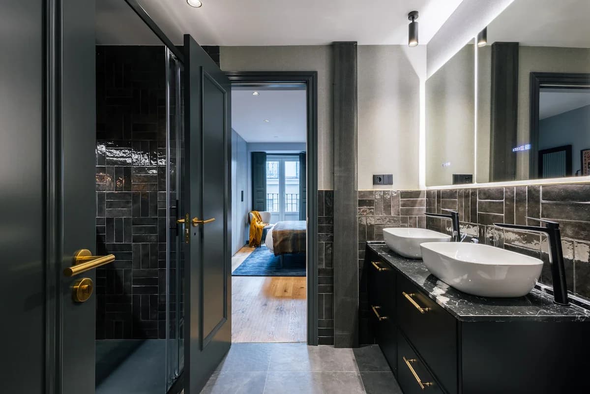 Black-tile ensuite with twin vessel sinks and view into bedroom