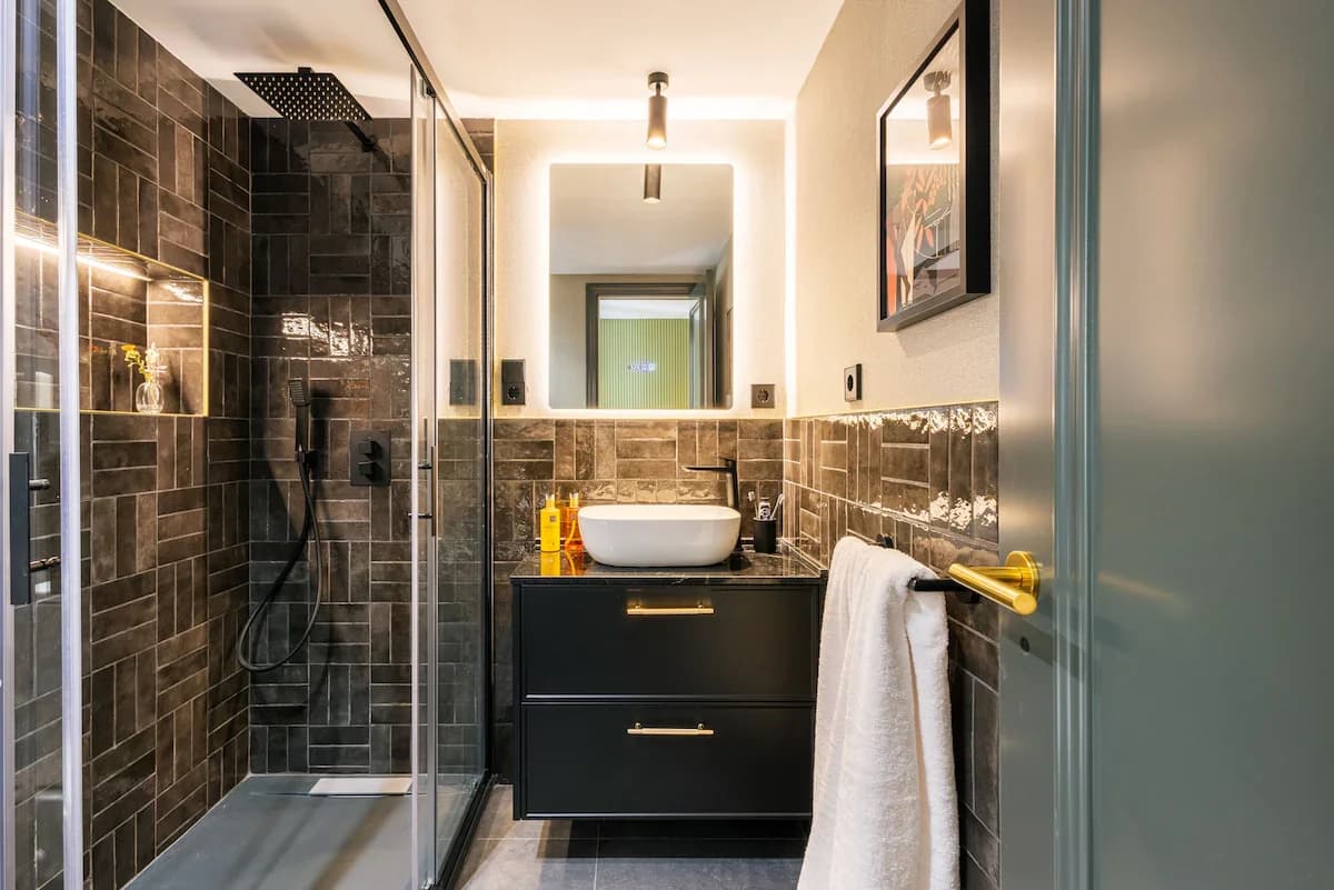 Compact ensuite with black tile shower and brass-handled vanity