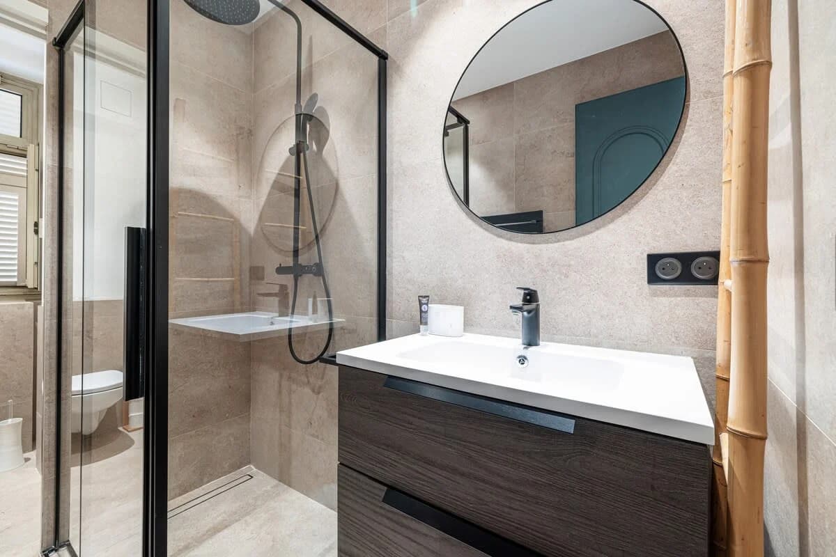 Stone-tiled bathroom with round mirror, walk-in shower and bamboo accent