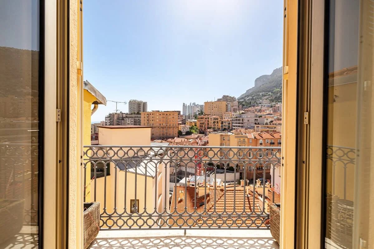 French balcony doors opening onto Monte-Carlo rooftops and rocky hillside