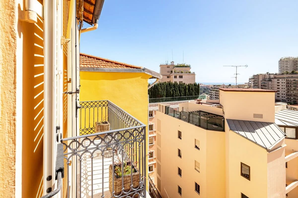 Wrought-iron balcony framed by yellow stucco walls and distant sea sliver