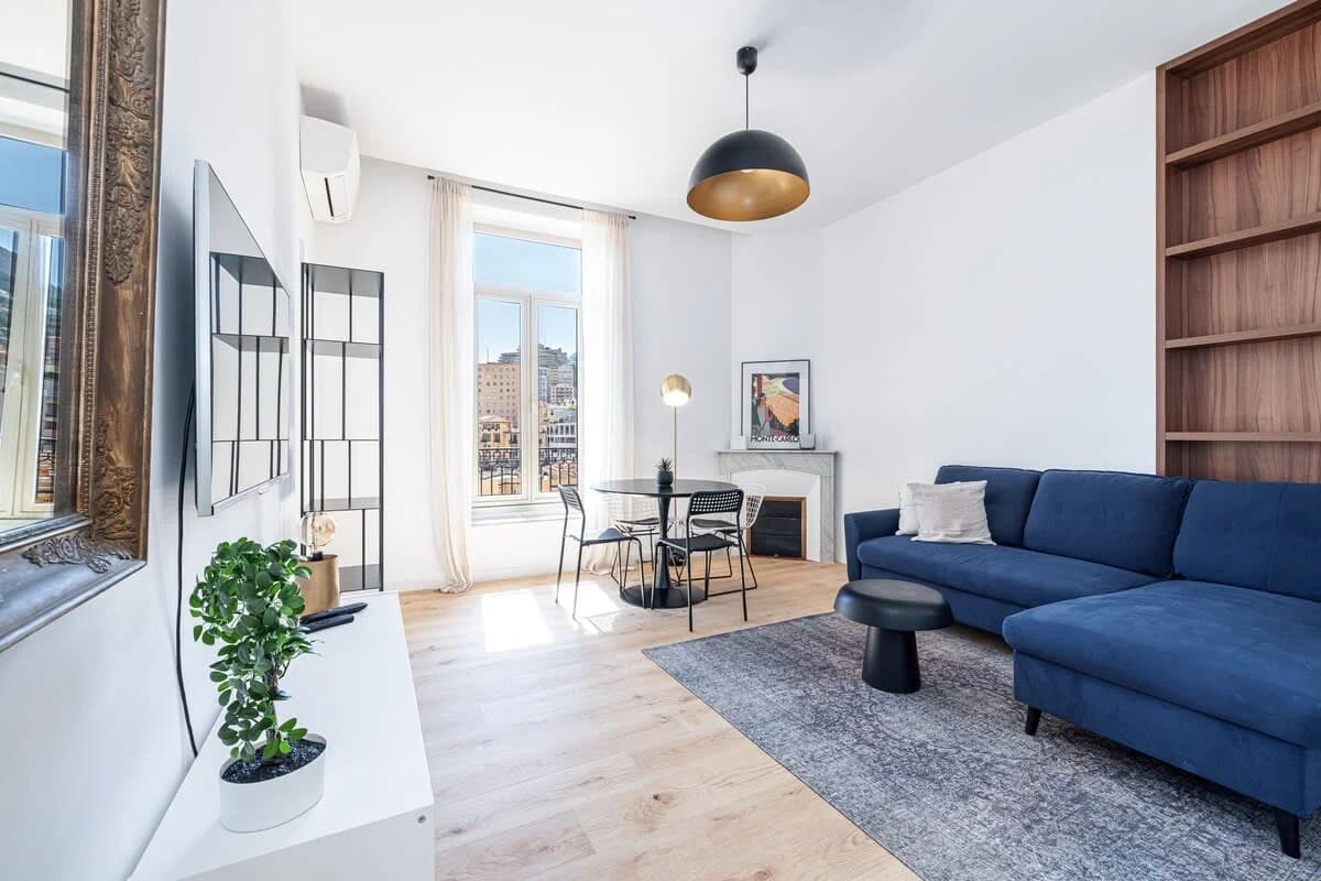 Bright living room with navy sectional, arched window framing Monaco rooftops
