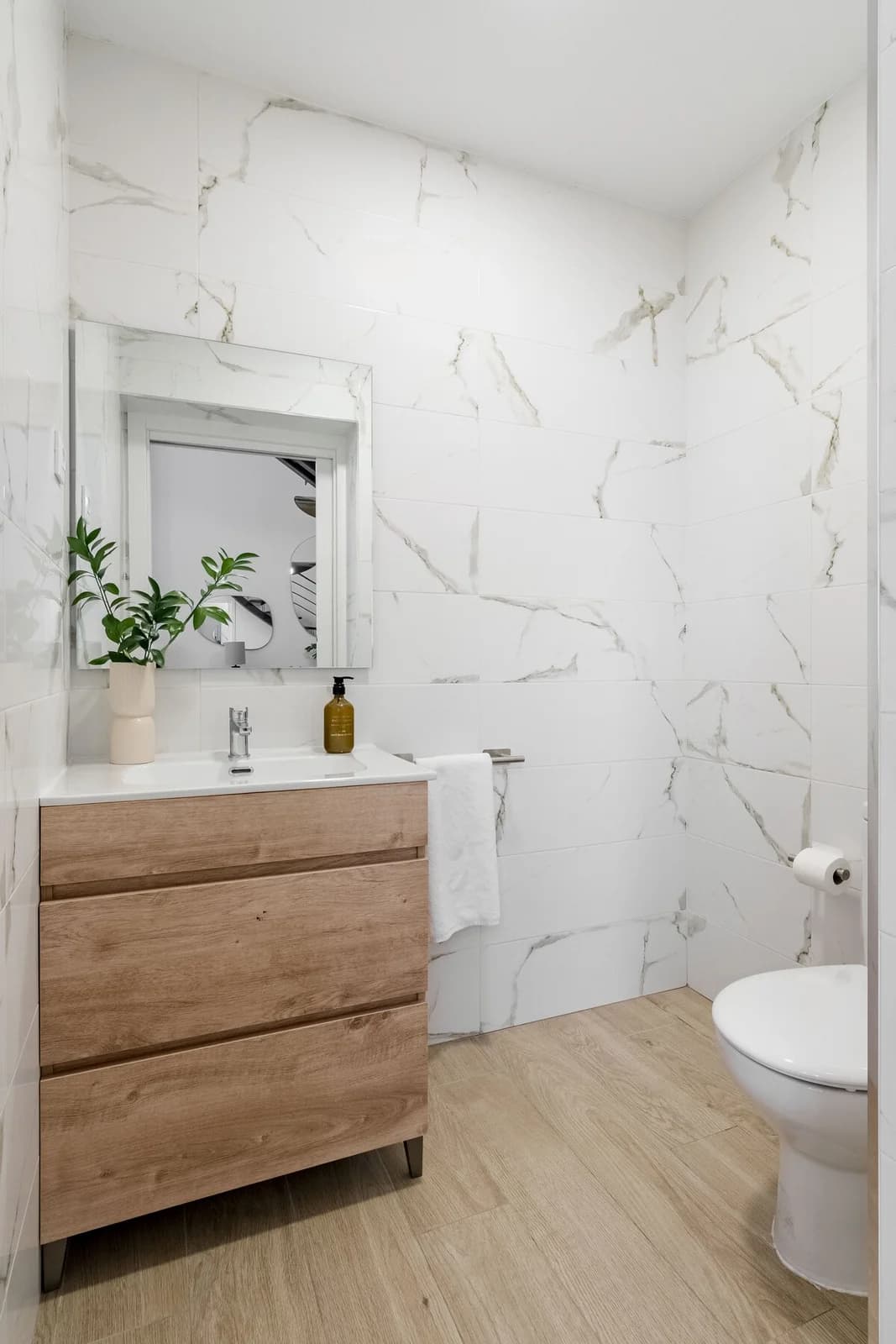 Veined marble bathroom with oak vanity and mirrored stairwell glimpse